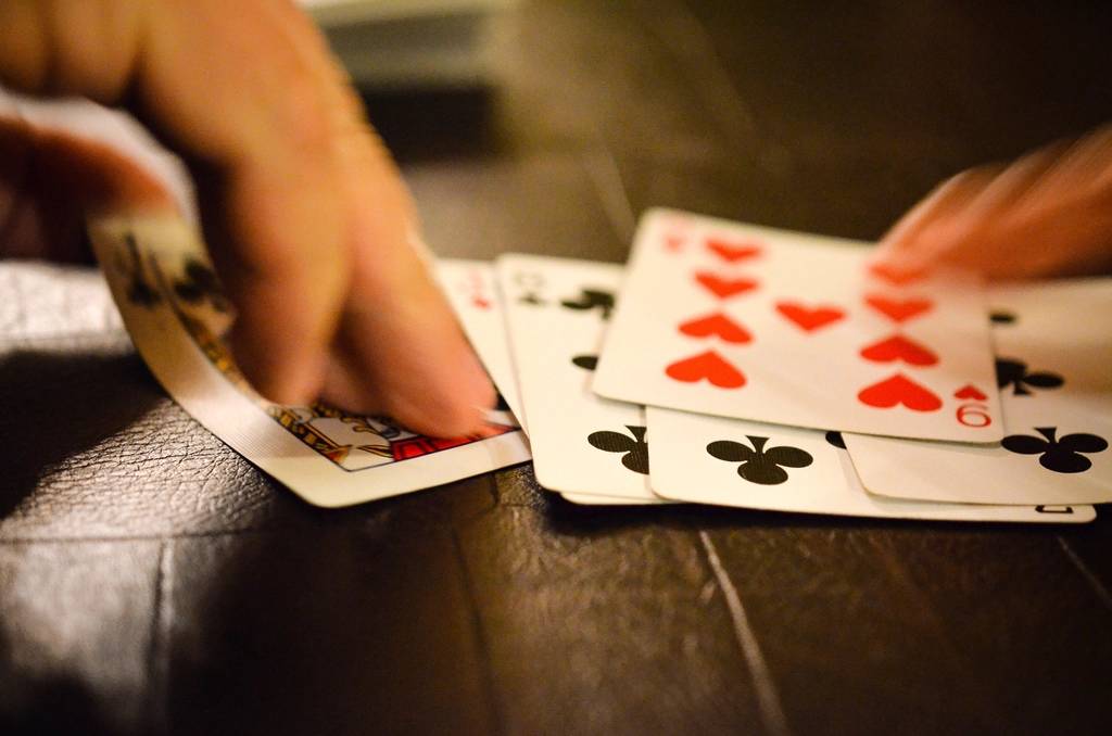Tangan pemain memegang kartu remi tersusun di atas meja poker
